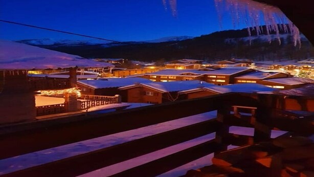 Un pueblo cubierto de nieve con edificios iluminados y montañas al fondo.