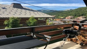 Un balcón con una parrilla, una mesa y vistas a un pueblo con casas y montañas.