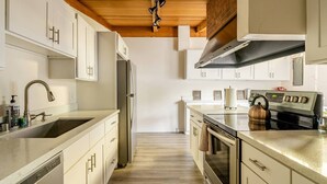 Una cocina moderna con armarios blancos, electrodomésticos de acero inoxidable y techo de madera.