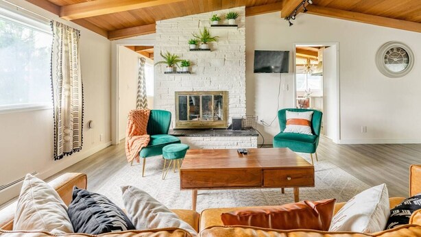 Una sala de estar con chimenea, sillones verdes, una mesa de centro de madera y un televisor instalado en la pared.