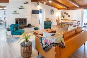A modern living room with a sofa, chairs, a coffee table, a fireplace, and a dining area.