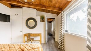 Un dormitorio con cama, escritorio, silla, espejo y ventana con cortinas.