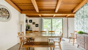 Un comedor con una gran mesa y sillas de madera, techo de madera y vistas a través de un ventanal.