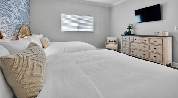 A bedroom with two large beds, a dresser, a chair, a window with blinds, and a wall-mounted TV.