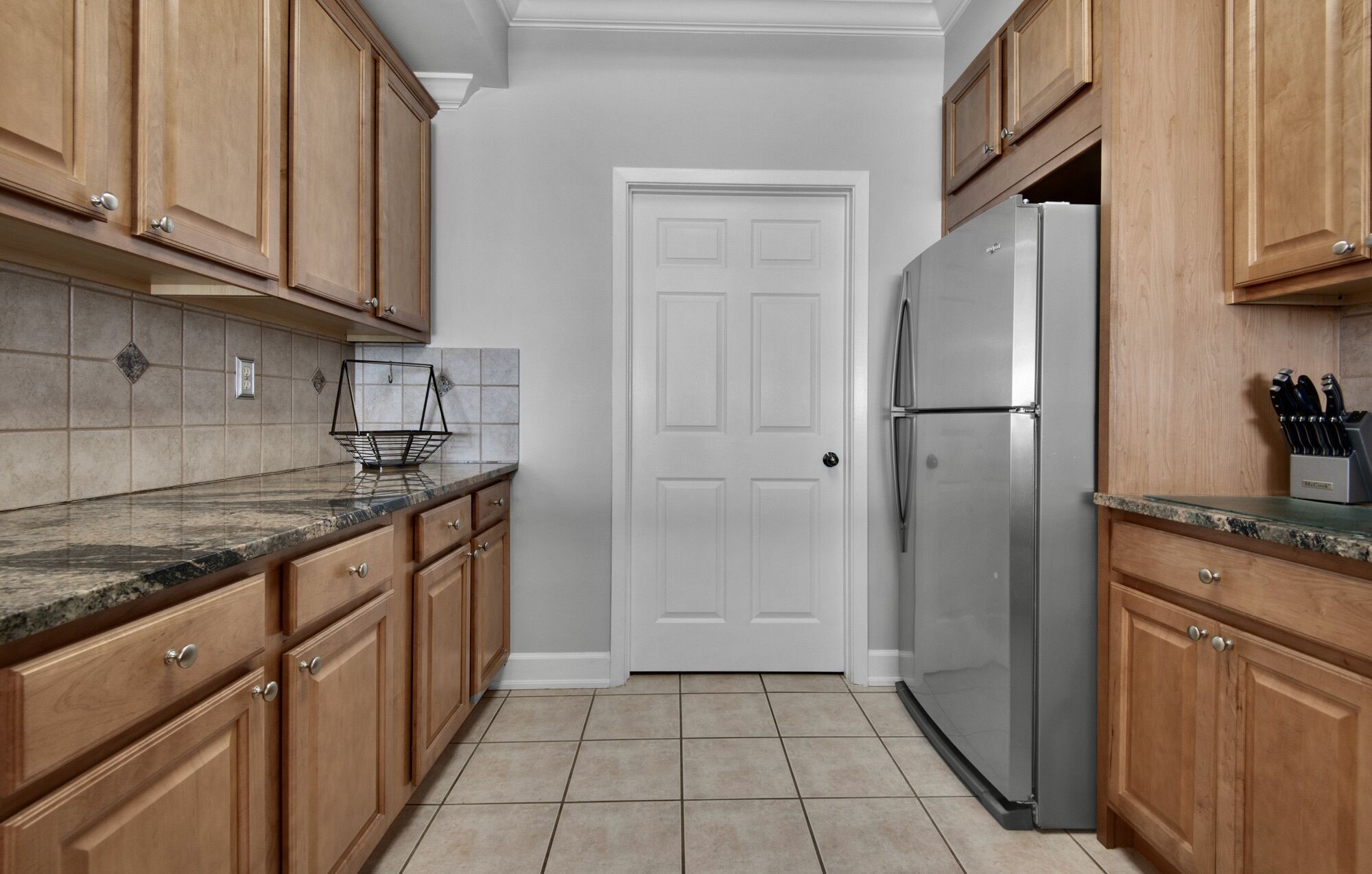 A kitchen with wooden cabinets, a stainless steel refrigerator, and a tiled backsplash.