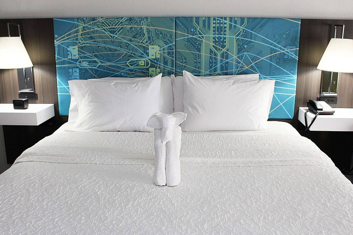 A hotel room with a large bed, two bedside tables, a wall-mounted TV, and a towel on the bed.