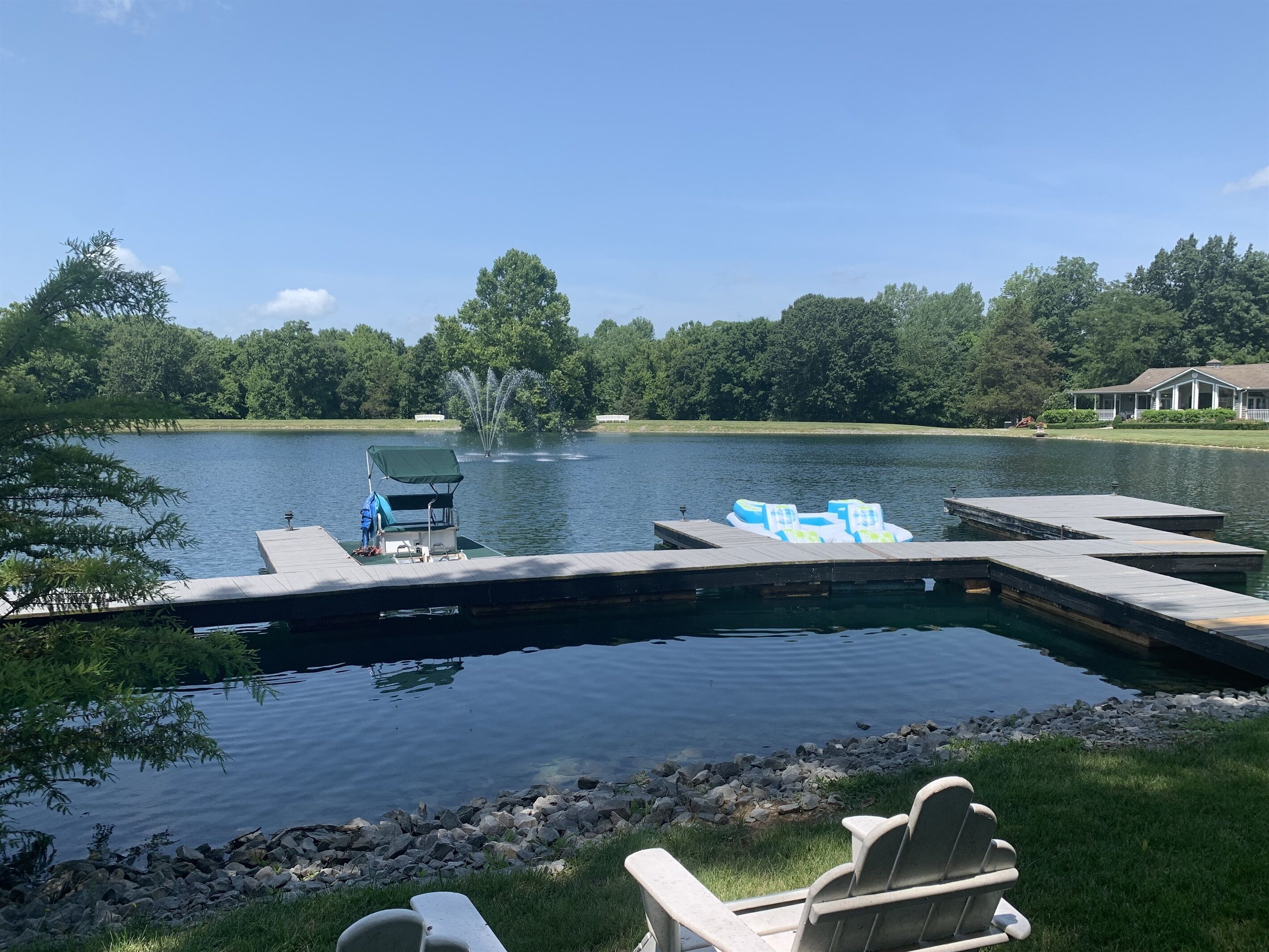 A lakeside dock with a boat, chairs, and a fountain.