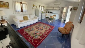 Un espacio habitable compacto con un sofá blanco, una alfombra estampada y una zona de cocina con una mesa y sillas.