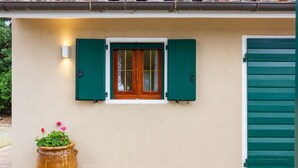 Un edificio con una ventana y una puerta verde, una planta en maceta y una lámpara.