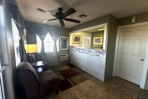 A living room with a ceiling fan, a couch, a rug, and a kitchen area with a counter and cabinets.