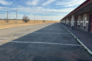 A long row of motel rooms with a parking lot in front.