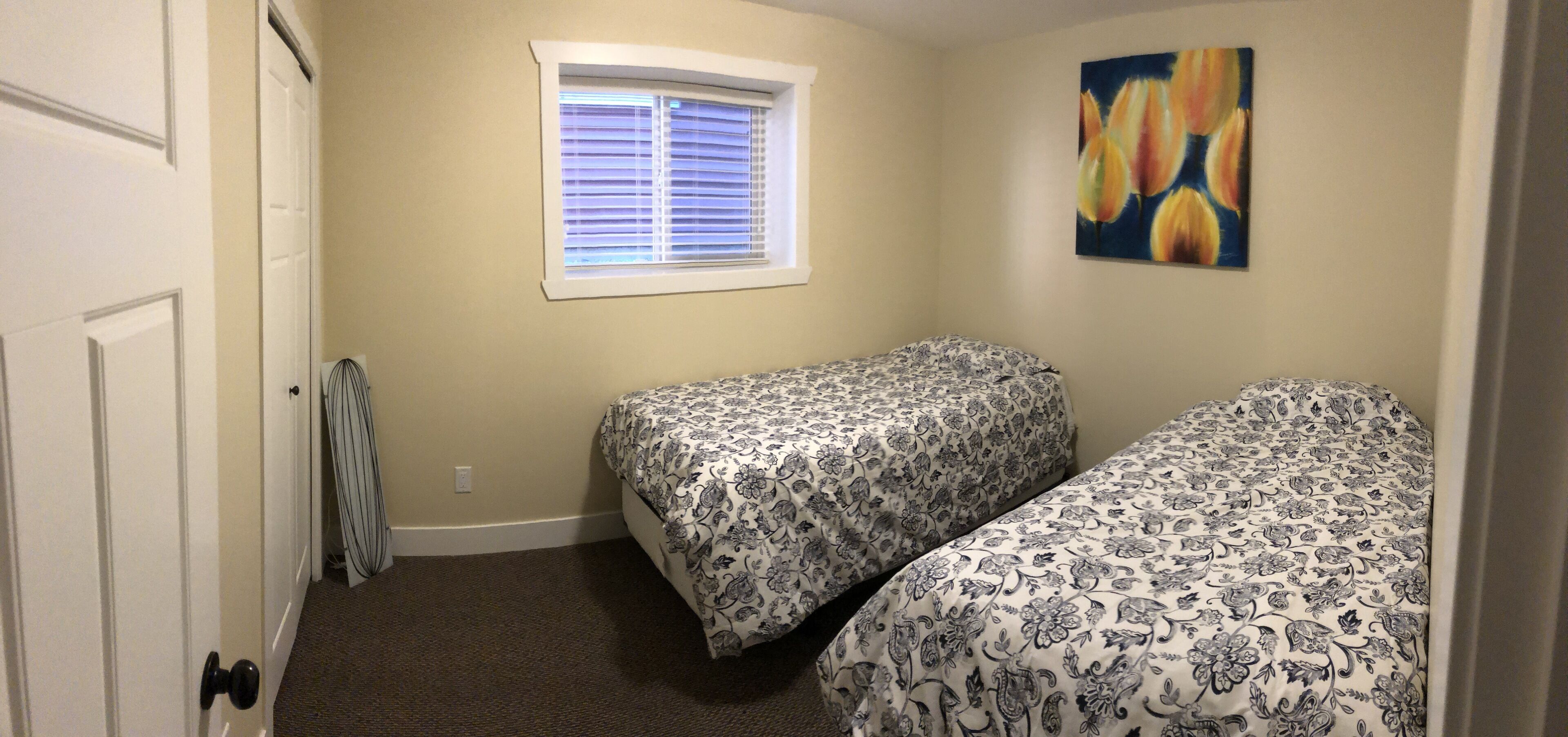 Une petite chambre propre, avec deux lits simples, une fenêtre avec des stores et un tableau au mur.