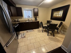 Une cuisine de taille réduite, dotée de meubles sombres, d’un réfrigérateur, d’un évier et d’un coin repas avec des chaises et une table.