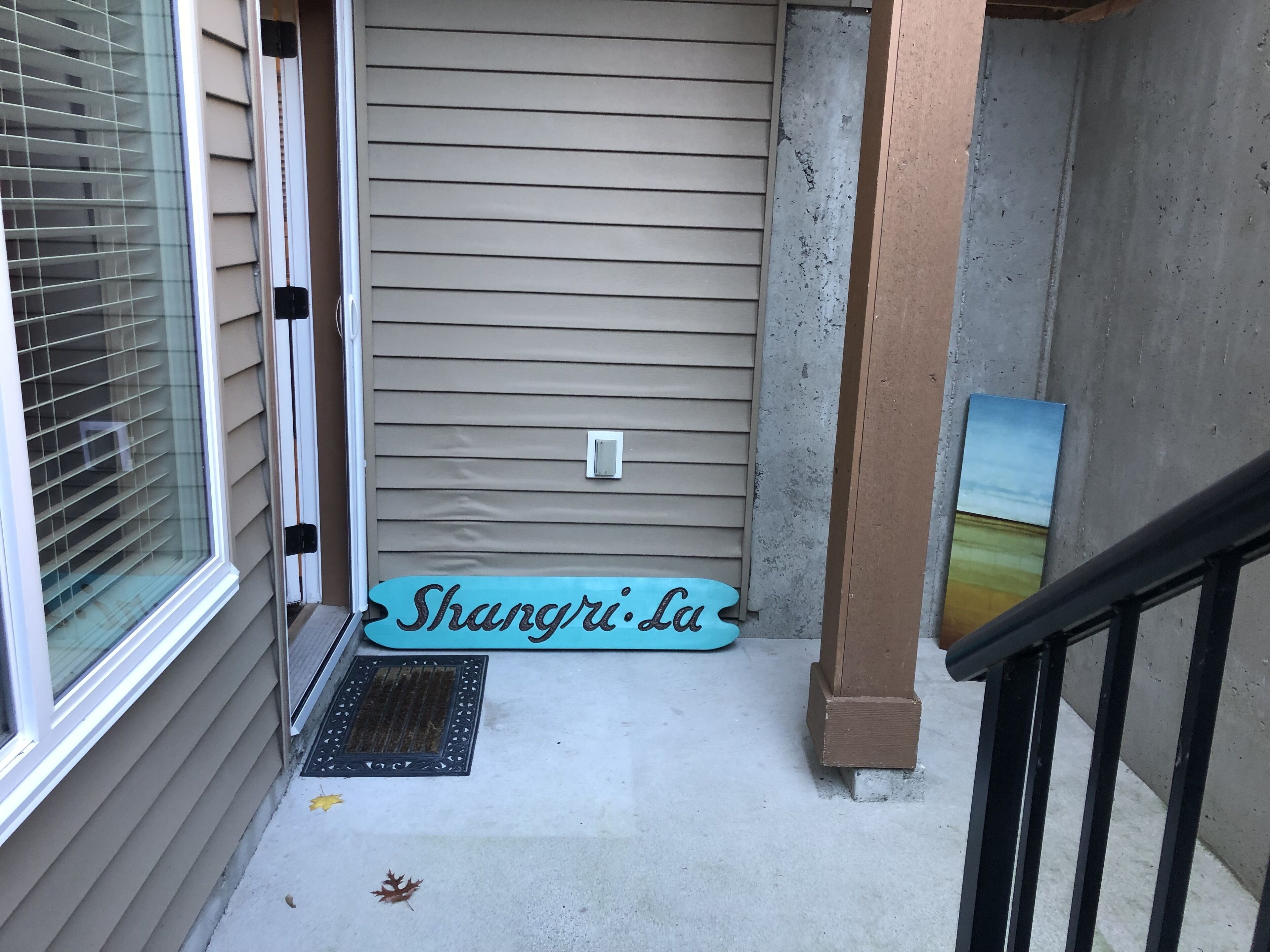 A residential entryway with a sliding glass door, a metal doormat, and a blue sign with the text "Shangri-La".