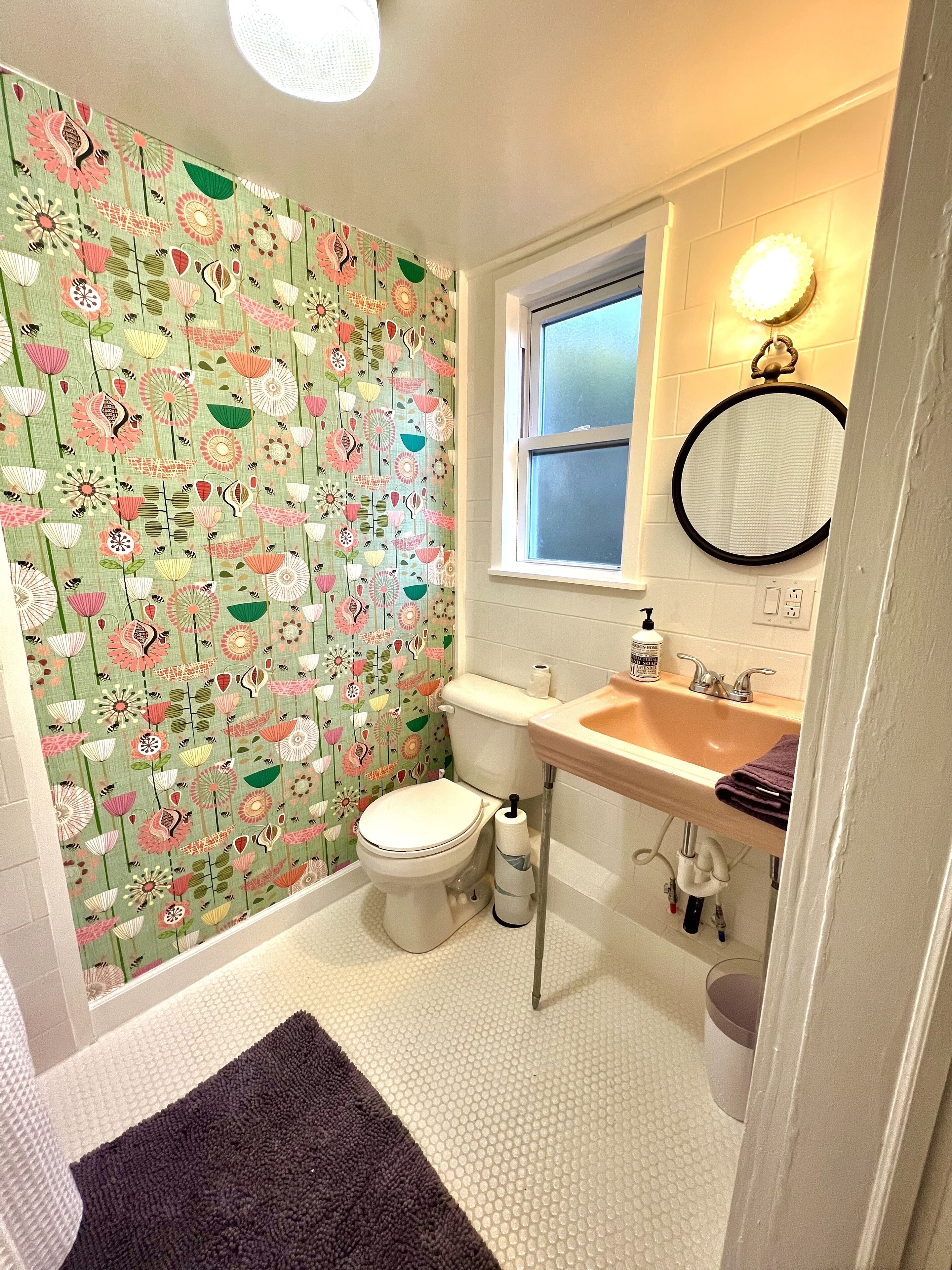 Un baño con inodoro, lavamanos y espejo. Las paredes tienen un estampado floral.