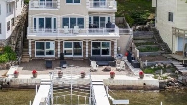 Una casa de dos pisos con un balcón, un muelle que se adentra en el agua y un pequeño jardín con plantas en macetas.