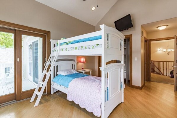 A bunk bed room with a ladder, a TV mounted on the wall, and a staircase leading to another level.