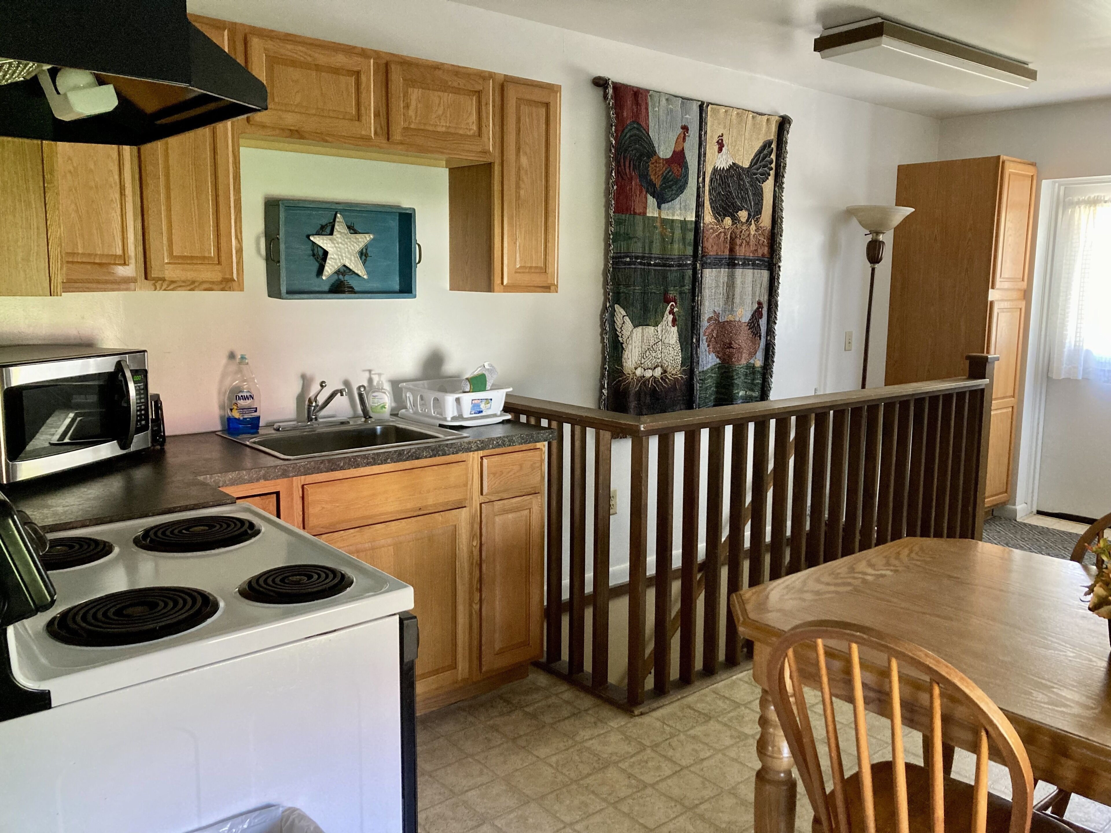 A kitchen with wooden cabinets, a microwave, a stove, a sink, and a dining area with a wooden table and chairs.