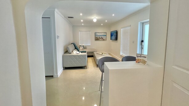 A modern, well-lit living area with a sofa, a dining table, and a TV mounted on the wall.