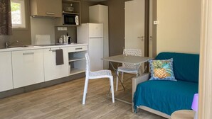 A compact living space with a kitchenette, a dining area, and a sofa with a decorative pillow. - Les Chalets des Îles Elba (Borgo)
