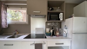 A compact kitchen with a microwave, refrigerator, and a window with curtains. - Les Chalets des Îles Elba (Borgo)