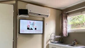 A compact kitchen with a built-in air conditioner, a flat-screen TV displaying a cat, and colorful shopping bags. - Les Chalets des Îles Elba (Borgo)