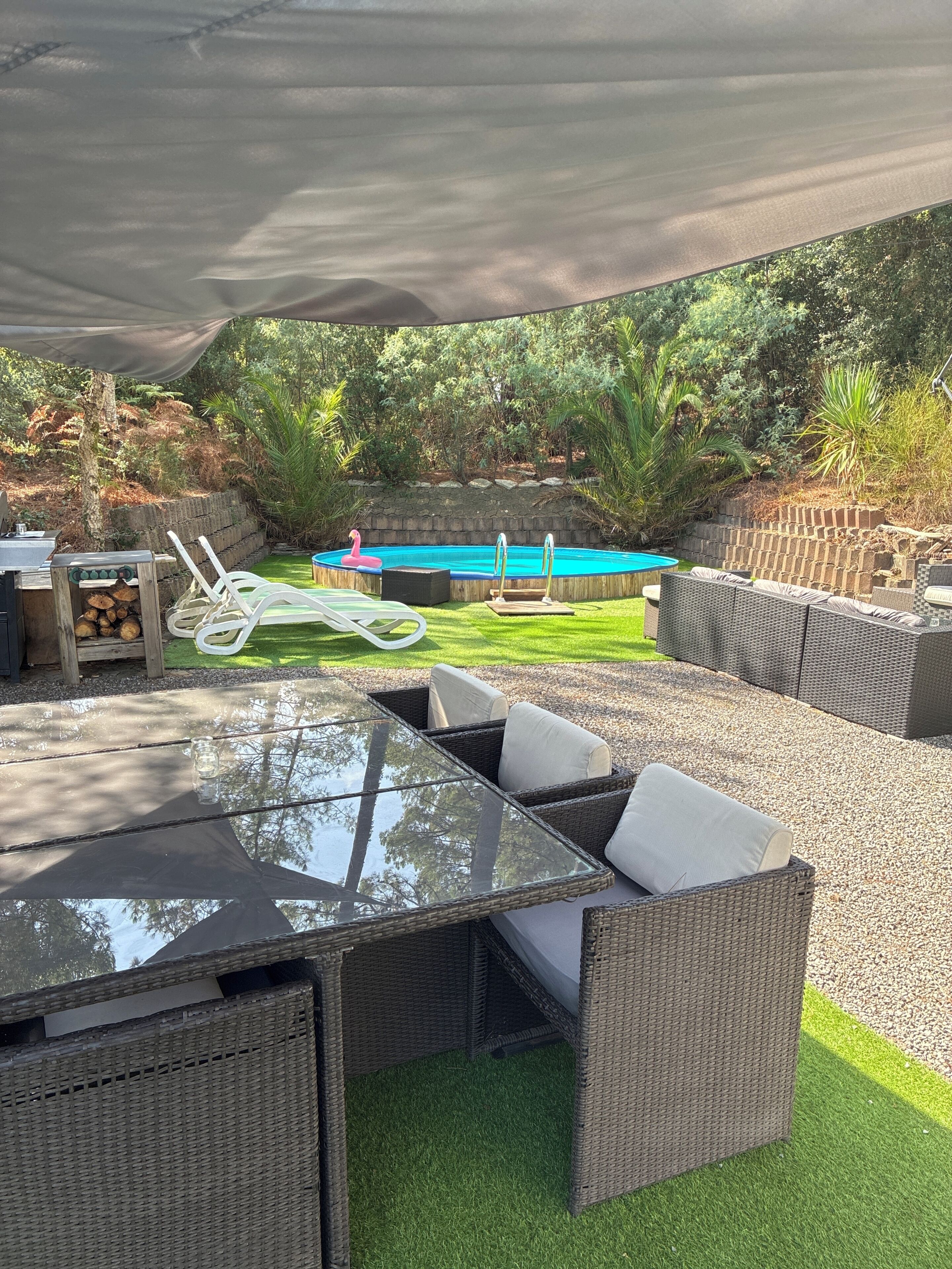 An outdoor patio with a glass-top table, wicker furniture, a pool, and a stone wall.