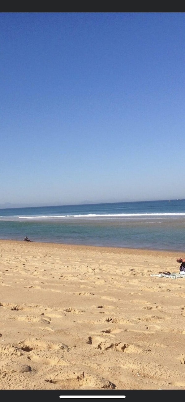 A beach with footprints leading to the water, a clear sky, and a calm sea.