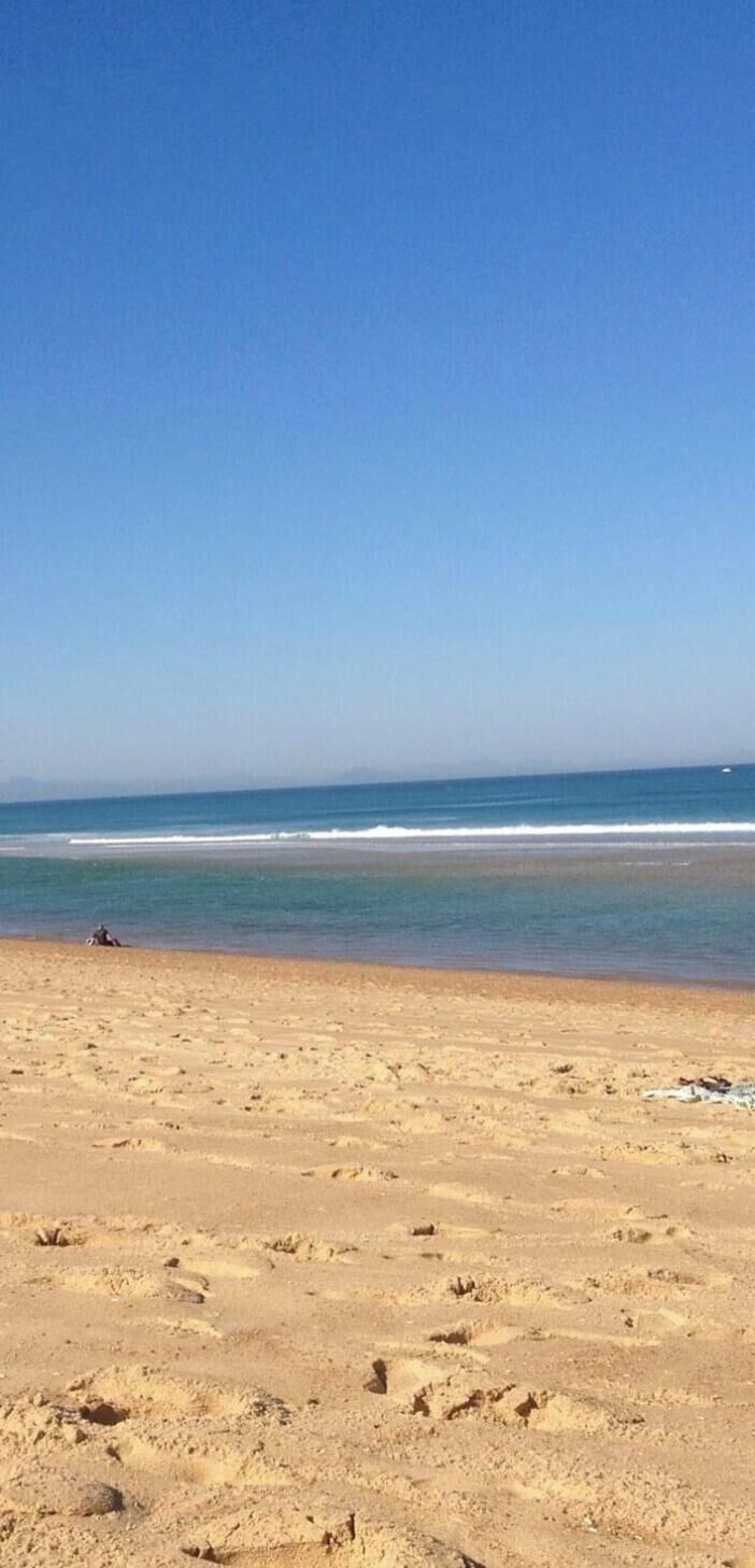 Une plage où l’on voit des empreintes de pas menant à l’eau, un ciel dégagé et une mer calme.