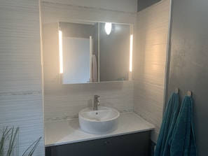 A bathroom with a white sink, a mirror, and two towels hanging on hooks.