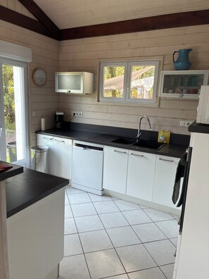 A kitchen with white cabinets, a black countertop, a dishwasher, a sink, and a window with a view of the outdoors.