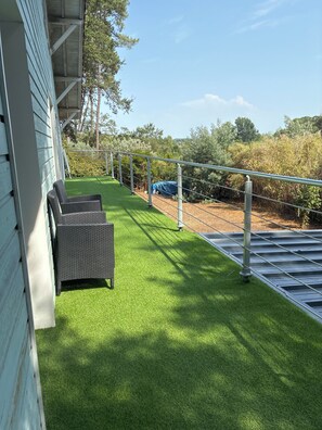 A patio with artificial grass, a metal railing, and a wicker chair.