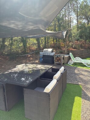 Un área de estar exterior con mobiliario de mimbre y una parrilla.