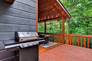 An outdoor deck with a built-in grill, wooden railing, and a table with chairs.