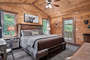 A wooden cabin bedroom with a bed, desk, chair, and a ceiling fan.