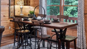 A wooden cabin interior with a dining table, chairs, a chandelier, and a window with a view of trees. - Stunning Mountain Modern Retreat! 3-Story/Location/Gameroom/Fireplace/Creek (Blue Ridge)