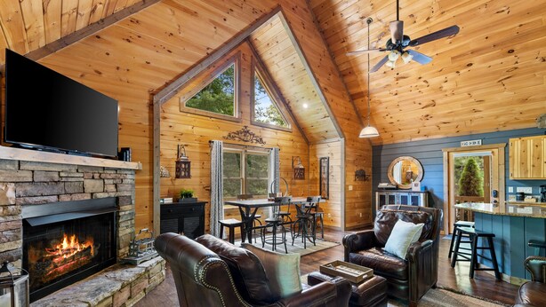 A cozy log cabin interior with a fireplace, leather furniture, a dining area, and a kitchen. - Stunning Mountain Modern Retreat! 3-Story/Location/Gameroom/Fireplace/Creek (Blue Ridge)