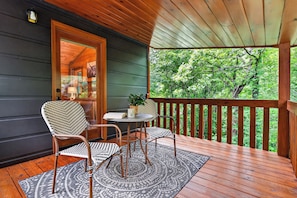 A wooden deck with a table and chairs, a rug, and a view of trees.