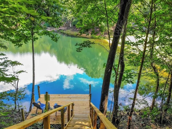 A wooden dock leading to a calm lake surrounded by dense green foliage.