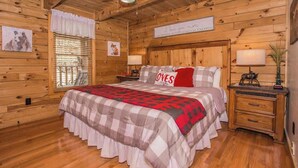 A wooden cabin bedroom with a bed, nightstands, a ceiling fan, and a window with blinds. - Cozy Cabin w/ Private Fishing Dock & Hot Tub (Sevierville)
