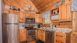 A kitchen with wooden cabinets, stainless steel appliances, and a marble countertop. - Cozy Cabin w/ Private Fishing Dock & Hot Tub (Sevierville)