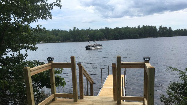Eine hölzerne Anlegestelle führt zu einem ruhigen See, in der Ferne ist ein Boot zu sehen.