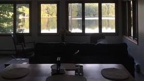 Ein Essbereich mit Tisch, Stühlen und Blick auf einen See durch große Fenster.