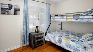 Une chambre avec un lit superposé, un panneau « Interdiction de fumer », un tableau encadré représentant un chat, une table de chevet avec une lampe et une literie à motifs.