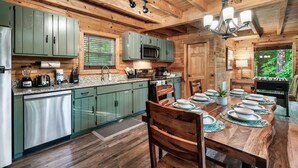 A wooden cabin-style kitchen with green cabinets, a built-in microwave, and a dining table set for four. - 15 Min. to Dollywood · Sauna · Hot Tub · Pool Table · Arcade • Foosball • Grill (sevierville)