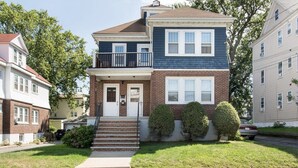 A two-story house with a front porch, a small balcony, and a garage. - Casa de Los Clarey • Boston • Logan   • Beaches • Free Parking (Winthrop)