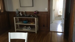 A room with a wooden floor, a white chair, a wooden console table with various items, a globe, and a door leading to another room. - Casa de Los Clarey • Boston • Logan • Beaches • Free Parking (Winthrop)