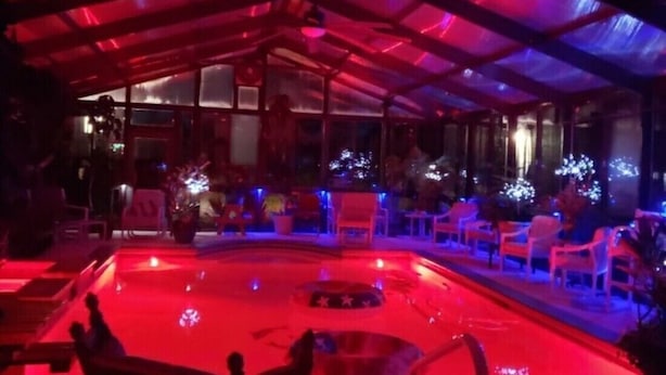 Un espace piscine extérieur abrité, doté d’un éclairage rouge, d’un aménagement avec des sièges et offrant une vue sur les environs.