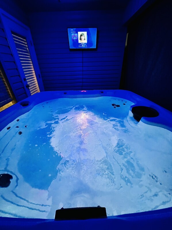 Un jacuzzi con una pantalla digital que muestra una foto de perfil y texto, rodeado de paredes azules y una puerta con vidrio ranurado.