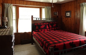 Une chambre dans un chalet en bois, avec un lit, un bureau et une fenêtre avec des rideaux.